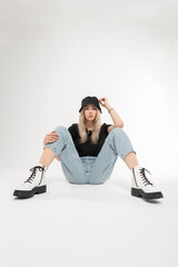 Pretty fashion young woman model with cool Panama hat in fashionable blue jeans, white stylish leather shoes and t-shirt sits on a white background. Cool beauty girl with trendy outwear