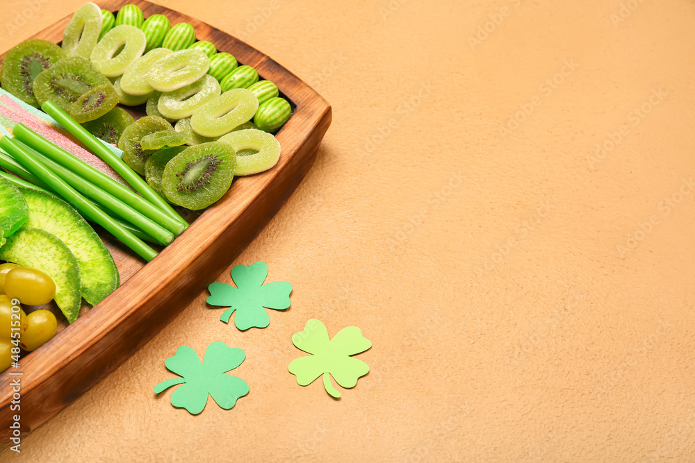 Wooden board with different sweets for St. Patrick's Day celebration on beige background, closeup