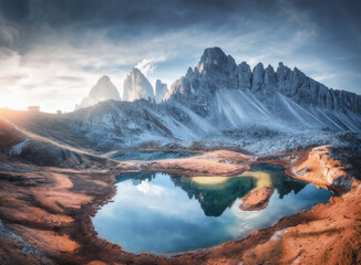 Wall Mural - aerial view of beautiful rocks, mountain lake, reflection in water and houses on the hill at sunset.