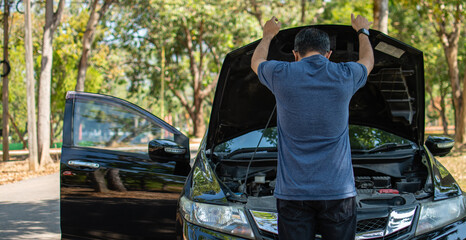 Man stands and inspects a broken-down car in a rural suburban forest. Black car, Engine won't start. Concept for roadside, damaged, stress, fix, problem. Close up, Selective focus, blurred background