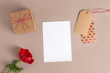 Wall Mural - Valentine day,Mother day composition made of gift, red flower, label paper with hearts, white blank card on beige background. Flat lay, top view, copy space.