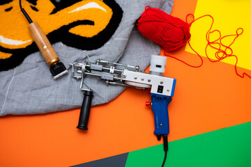 A tufting gun with multicolored yarns against a bright colored background.
