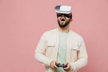 Canvas Print - Young happy man 20s wear trendy jacket shirt hold in hand play pc game with joystick console watching in vr headset pc gadget isolated on plain pastel light pink background. People lifestyle concept.