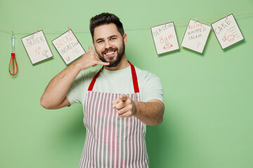 Poster - Young smiling fun happy friendly male chef confectioner baker man 20s in striped apron doing phone gesture like says call me back isolated on plain pastel light green background. Cooking food concept.