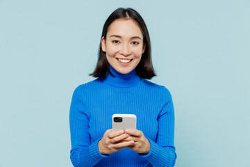 smiling fancy young woman of asian ethnicity 20s years old wears blue shirt hold in hand use mobile 