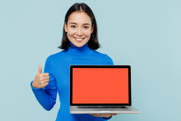 Young woman of Asian ethnicity 20s wears blue shirt use laptop pc computer with blank screen workspace area show thumb up like gesture isolated on plain pastel light blue background studio portrait.