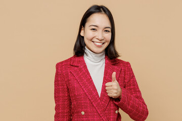 Wall Mural - Smiling satisfied cheerful fun happy woman of Asian ethnicity wear red jacket showing thumb up like gesture isolated on plain pastel beige background studio portrait. People lifestyle fashion concept.