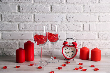 Wall Mural - Red candles, wine glasses, heart shaped alarm clock on a table against a white brick wall.