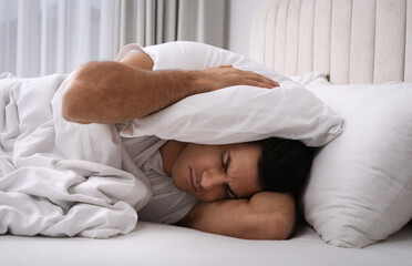 Canvas Print - Handsome man sleeping under pillow in bed at home