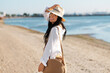 © Syda Productions - people, summer holidays and leisure concept - happy smiling woman in white shirt and straw hat with jute bag walking along beach