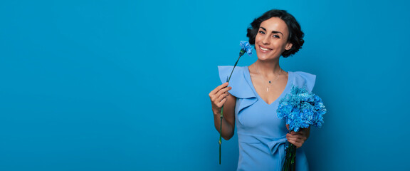 The portrait of a happy excited gorgeous young woman in an elegant blue dress is posing with a fresh bunch of blue flowers. Mothers day. Women's holidays. Springtime. Women rights