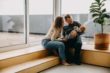 Happy young family at home. Mother and father holding newborn baby in arms, smiling, looking at him.