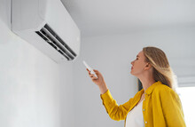 Woman Holding Remote Control Aimed At The Air Conditioner.