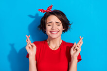 Photo Of Optimistic Millennial Brunette Lady Crossed Fingers Wear Red T-shirt Hairband Isolated On Blue Color Background