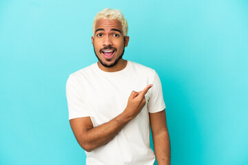 Wall Mural - Young Colombian handsome man isolated on blue background surprised and pointing side