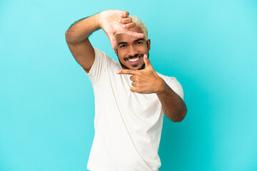 Wall Mural - Young Colombian handsome man isolated on blue background focusing face. Framing symbol