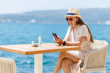 young lady in dress sitting at the table in cafe near the sea. young travel woman enjoying sunny day