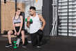 © LIGHTFIELD STUDIOS - Trainer holding dumbbell near blonde sportswoman in gym.