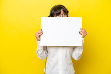 Telemarketer Latin Woman Working With A Headset Isolated On Yellow Background Holding An Empty Placard And Hiding Behind It