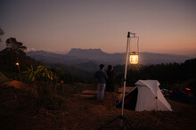 White Tent With Lantern Lighting And Tourists Man Standing Enjoy The Mountain Peak At The Sunset