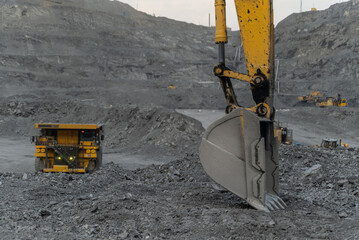 Wall Mural - Excavator bucket close-up. A moving dump truck can be seen in the background. The action takes place in an open pit.