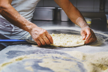 The Italian pizza maker prepares a margherita pizza by rolling out the dough with mozzarella on the work surface before cooking in the stone oven