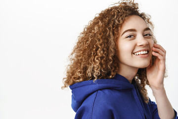 Close up portrait of beautiful curly girl with happy smile, wearing blue hoodie, looking at camera cheerful, standing against white background