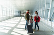 © NFstock - Full length view of the happy family of mother, father and daughter walking with suitcases to the departure lounge. Traveling and journeys concept