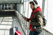 © NFstock - Side view of the tourist man wearing casual clothes listening music via headphones while leaning at the window and waiting for his flight. Stock photo