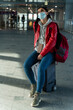 © NFstock - Full length view of the woman wearing protective mask looking up while sitting at her baggage and waiting for plane. Traveling and adventures concept