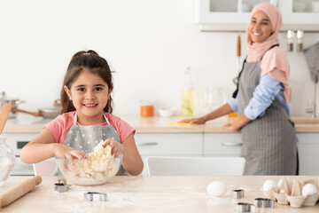 Wall Mural - Cute Female Child Preparing Dough While Baking With Muslim Mom In Kitchen