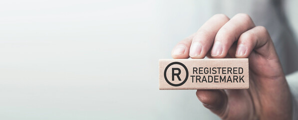 male hand showing r-registered trademark on wooden block.