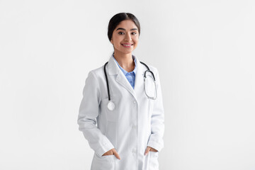 Wall Mural - Portrait of confident smiling millennial indian female doctor in white coat with stethoscope