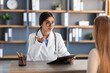 © Prostock-studio - Friendly millennial indian woman doctor therapist in white coat and glasses consultations client in clinic