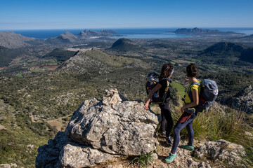 hikers ascending cucuia de fartaritx with alcudia bay in the background, pollença, mallorca, baleari