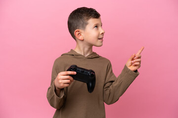 Little caucasian boy playing with a video game controller isolated on pink background pointing up a great idea