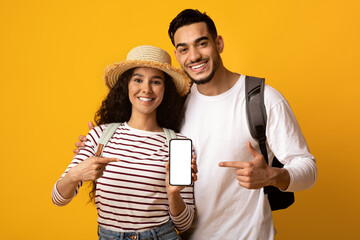 Wall Mural - Cheerful Middle Eastern Travellers Couple Pointing At Smartphone With Blank Screen