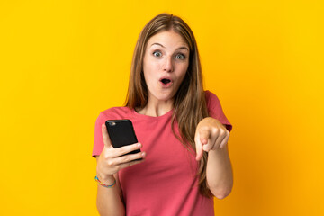 Canvas Print - Young woman using mobile phone isolated on yellow background surprised and pointing front