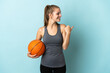 © luismolinero - Young woman playing basketball isolated on blue background pointing to the side to present a product