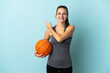 © luismolinero - Young woman playing basketball isolated on blue background pointing to the side to present a product