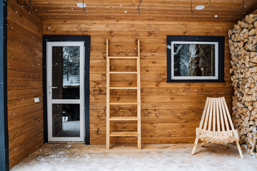 Garden chaise longue for outdoor seating made of wood. Logs. Chopped birch firewood in a log. Wooden staircase against the wall. Modular house with plastic windows