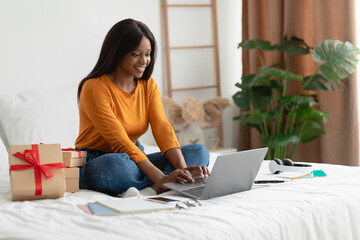 Wall Mural - African Woman Using Laptop Sitting Near Gifts Boxes In Bedroom