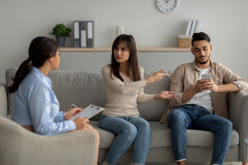 Wall Mural - Irritated arab woman complaining about her husband's smartphone addiction during psychological consultation