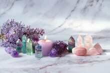 Gemstones Minerals, Candle, Lilac Flowers On Marble Background. Healing Stones For Crystal Ritual, Esoteric Spiritual Practice, Aura Cleansing, Relax. Reiki Therapy. Fluorite, Amethyst, Rose Quartz