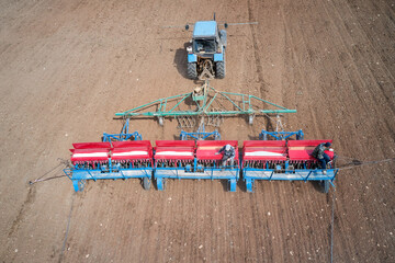 Tractor with a seeder on arable land. Grain and mineral fertilizer are filled into the seeder bunkers. Two farmers are sitting on the seeder. Close-up.  Shooting from a drone.