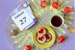 Calendar for February 27: the name of the month February in English, the numbers 27 on the loose-leaf calendar, a cup of tea, heart-shaped cookies, physalis branches on a yellow openwork napkin