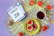 Calendar for February 28: the name of the month February in English, the numbers 28 on the loose-leaf calendar, a cup of tea, heart-shaped cookies, physalis branches on a yellow openwork napkin