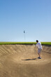 Golfing middle aged man, hitting golf ball out of the sand trap bunker. Photo taken from inside bunker with clear blue sky in background. Copy space.