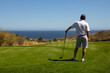 Middle aged man wearing golf shorts and golf shirt, looking out over ocean side tropical golf course view while waiting to tee off. Copy space.