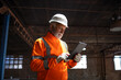 Professional senior heavy industry engineer worker wearing safety uniform and hard hat, using tablet computer controlling production.
